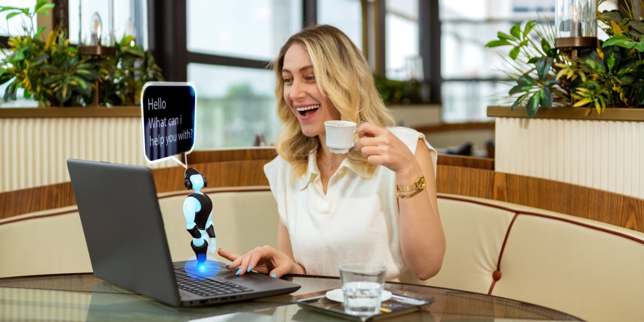 A young white blonde woman sits at her laptop smiling and holding a coffee cup while a computer generated miniature robot stands on her laptop. A speech bubble reads hello what can I help you with.  The room is edged by windows with green plants